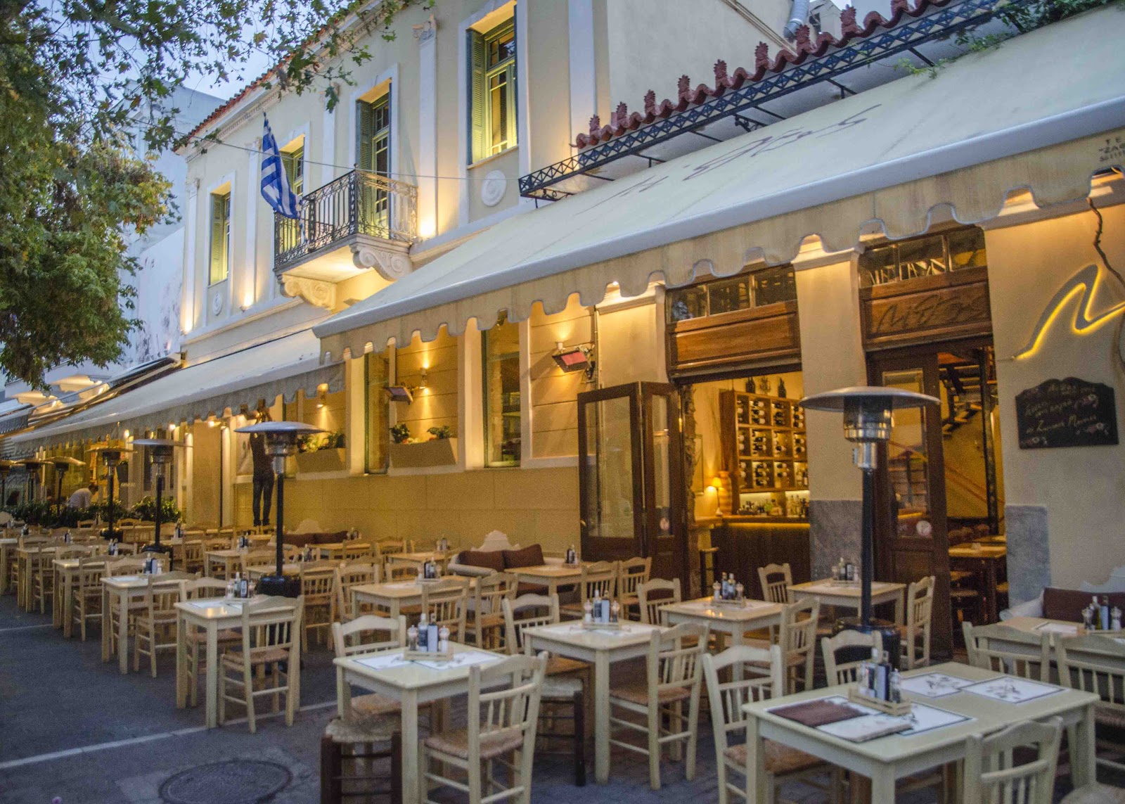 Stone-walled Greek taverna interior with warm lamps and wooden tables in Psiri Athens