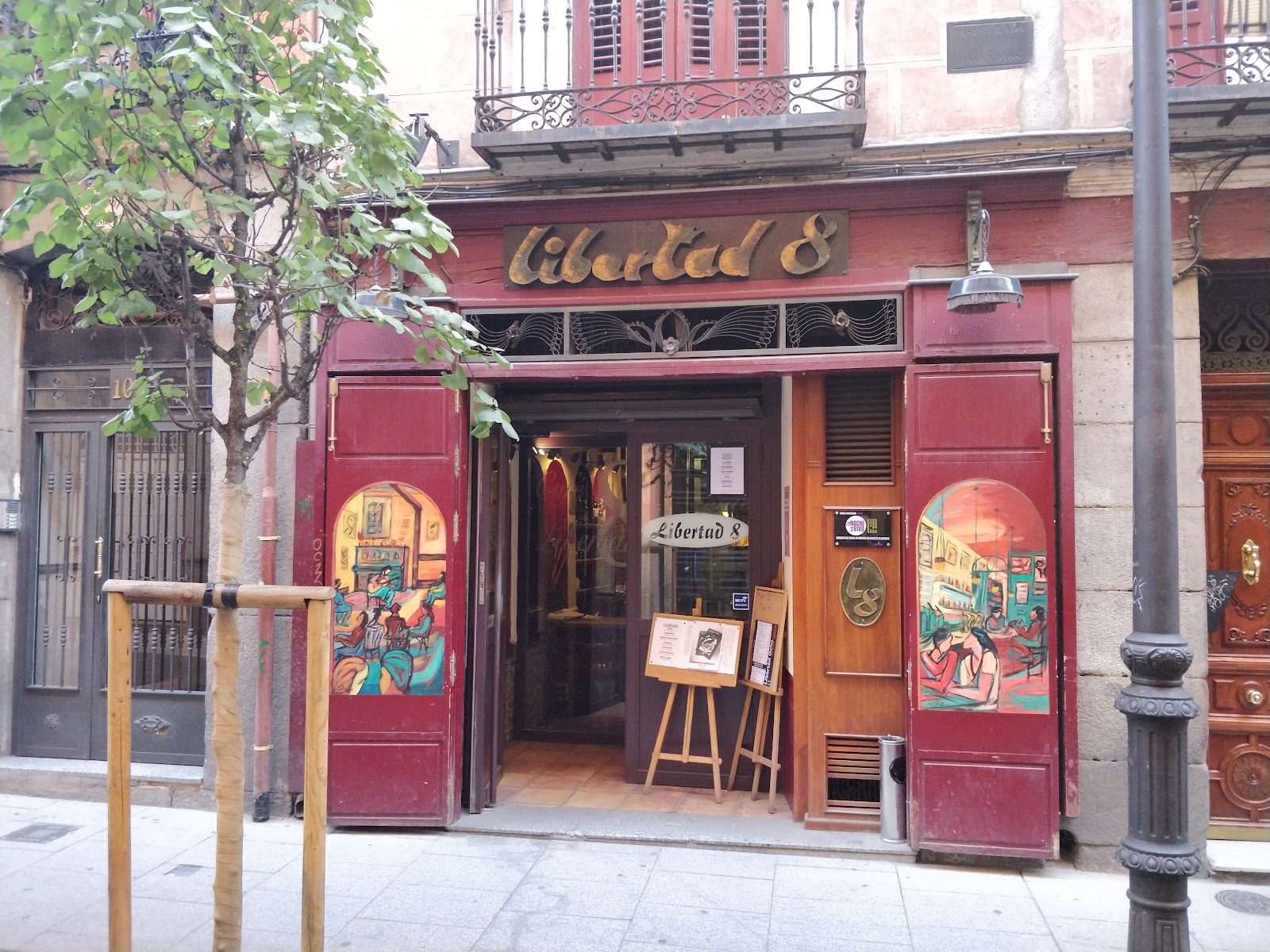 A small live music room with a low stage and warm light, in the style of Café Libertad 8, Chueca, Madrid